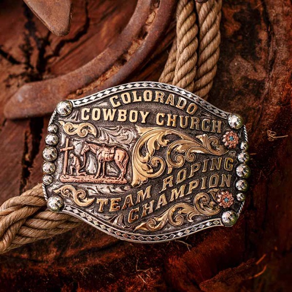 A custom western belt buckle trophy for Colorado Cowboy Church Team Roping Champion featuring a praying cowboy figure 